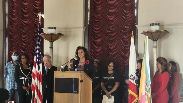 Capri Maddox stands at a podium in the Tom Bradley Tower of LA City Hall with Council President Paul Krekorian, members of the LA Black Worker Center, and Commissioners on the Los Angeles Civil Rights Commission